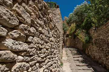 View of typical stone houses and wall with sunny blue sky, in alley of the historical city center of Gordes. Provence region, southeastern France.