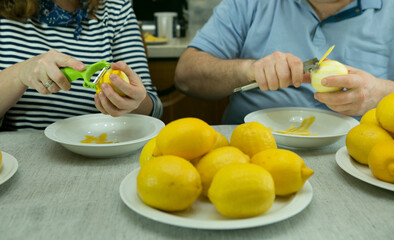 The process of making limoncello lemon liqueur at home. A man and a woman removes the zest from the...