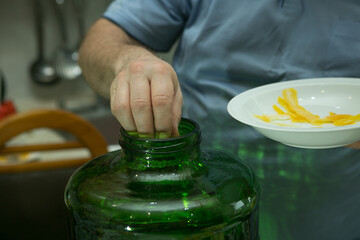 The process of making limoncello lemon liqueur at home. A man adds prepared fresh lemon zest to a...