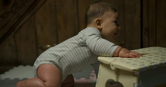 A little baby is using a foot stool to pull himself up to stand