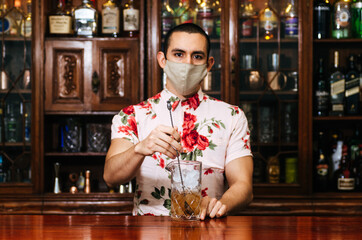 Barman pouring whiskey wearing protective mask on the bar counter