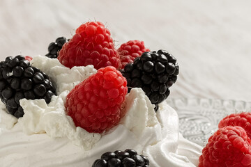 Pavlova's cake, decorated with raspberries and blackberries. Light wooden background. Home cooking.