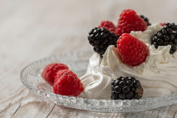Pavlova's cake, decorated with raspberries and blackberries. Light wooden background. Home cooking.