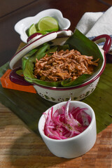 cochinita pibil tacos on a bowl with banana leaves, red onion and lemon. cochinita pibil is a traditional Mexican dish of slow roasted marinated pork.