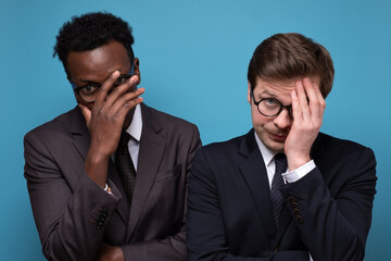 Feeling depressed after work. Exhausted young men covering face with hand. Studio shot on blue wall.