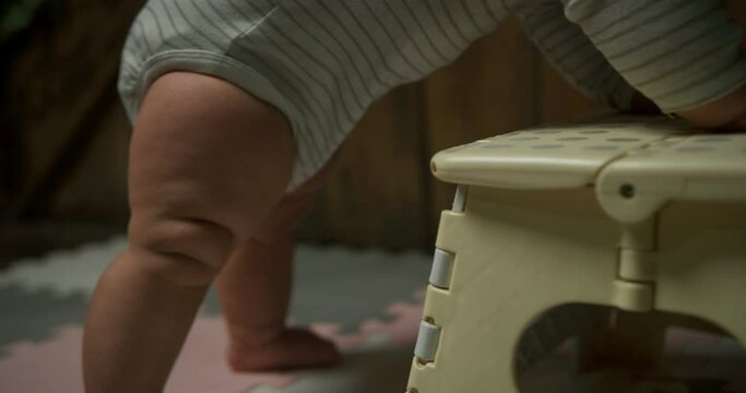 A little baby is using a foot stool to stand up and move around