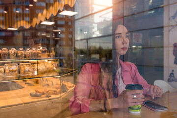Woman in summer in a city cafe. Free space for a copy of text. Background of coffee tea pastries and showcase, smartphone on table. Rest and lunch after work, breakfast break.