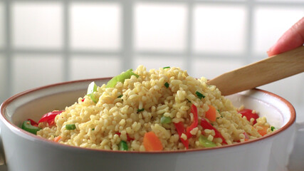 A wooden spoon is inserted into the bulgur plate with vegetables and the bulgur is aired.