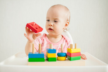 little girl plays with an educational toy - a multi-colored wooden pyramid. Development of fine motor skills and logical thinking. High quality photo