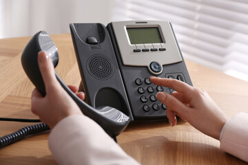 Woman using desktop telephone at wooden table in office, closeup. Hotline service