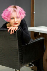 Portrait of a beautiful young caucasian woman with new short pink hairstyle sitting in a chair at a...