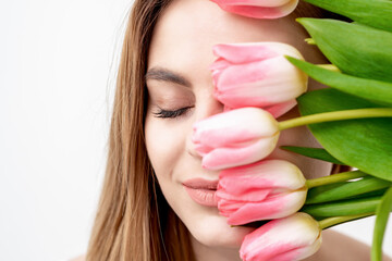 A portrait of a happy young caucasian woman with closed eyes and pink tulips cover her face against a white background