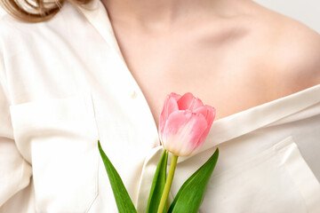 Obraz na płótnie Canvas One pink tulip against on background of a young female wearing a white shirt