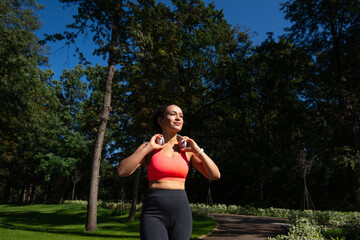 Sporty young woman with headphones on the neck walking on a running way in the park after workout