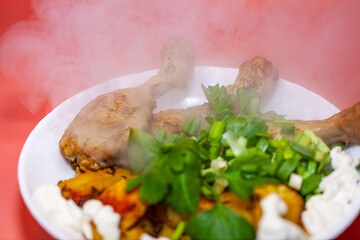 Fried chicken thighs with fried potatoes and greens on a pink background