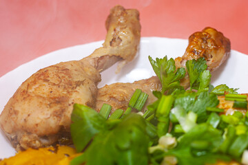 Fried chicken thighs with fried potatoes and greens on a pink background
