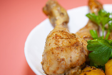 Fried chicken thighs with fried potatoes and greens on a pink background