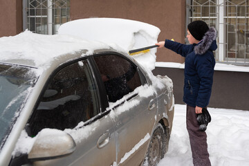 kid helps to clear the car of snow