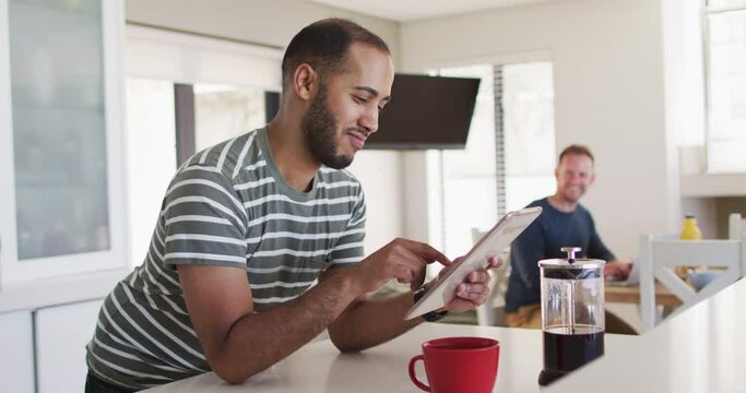 Multi ethnic gay male couple in kitchen one using tablet