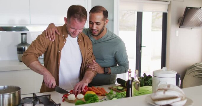 Multi ethnic male same sex couple preparing food and talking in kitchen