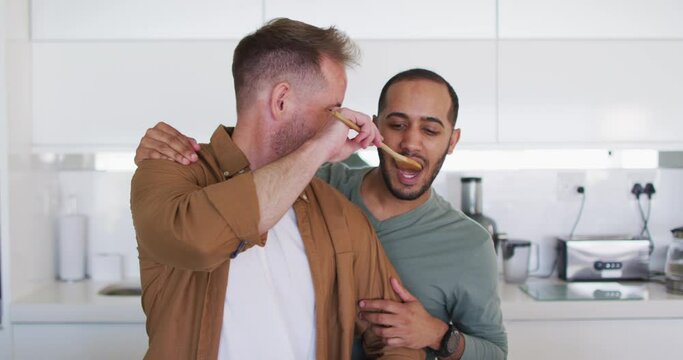 Multi Ethnic Male Same Sex Couple Preparing Food And Tasting In Kitchen