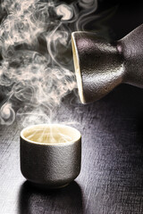 black oriental style cup, used for drinking sake or hot tea. Hot steam rising. Black background...