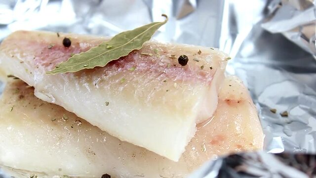 Raw pollock fillet on foil with salt, pepper and bay leaf. Close-up, selective shot.