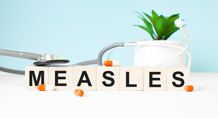 The word measles is written on wooden cubes near a stethoscope on a wooden background. Medical concept