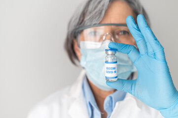Portrait of a scientist or senior female doctor, WHO representative in medical latex gloves holding a covid-19 coronavirus vaccine. The successful vaccination development, ready for the trial concept