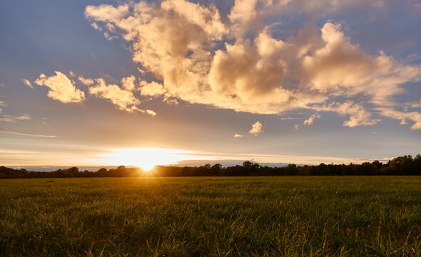 Beautiful sunset in the evening, gray clouds against a blue sky, green meadow in the foreground, depth of field. Germany, Ostfildern.