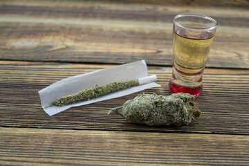 Joint, grinder, cannabis buds, alcohol shot and related items on a table.