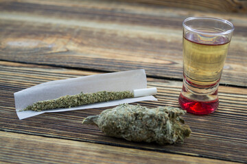 Joint, grinder, cannabis buds, alcohol shot and related items on a table.
