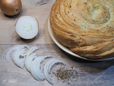 Uzbek flatbread fatir with onion, sesame seeds and cumin on a wooden background, closeup, flat layout. Traditional Asian pita made of wheat flour, puff pastry with spices. Bakery of oriental cuisine