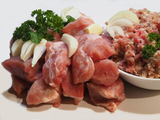 Fresh raw meat, cut into pieces with onions and spicy herbs and minced meat in a bowl on a white background, closeup. Prepared natural meat pork for cooking shish kebab and ground meat