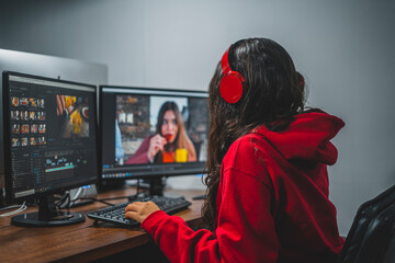 Mujer joven editando video en dos monitores con audífonos  sudadera roja