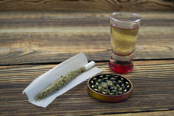 Joint, grinder, cannabis buds, alcohol shot and related items on a table.