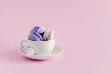 Cup with french macarons and marshmallows on a pink pastel background.