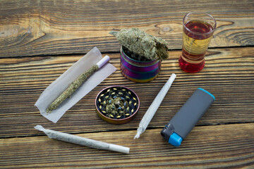 Fototapeta na wymiar Joint, grinder, cannabis buds, alcohol shot and related items on a table.