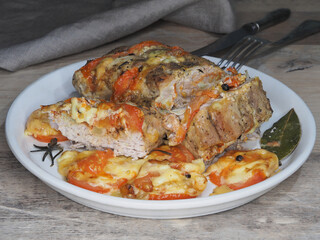 Roast pork with cheese and tomatoes in a plate, napkin, cutlery on the table, closeup. Quick recipe for a hot meat dish with vegetables for lunch