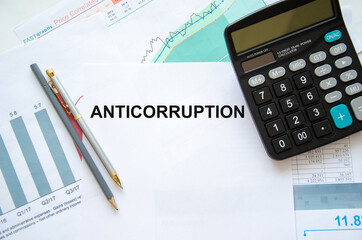 anticorruption text is written on a white sheet of paper that lies on a financial chart near a calculator and pens