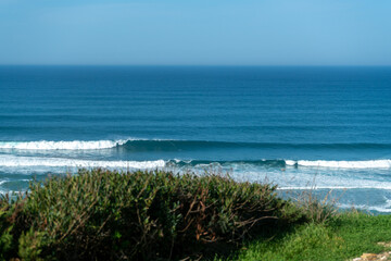 Coastline with vegetation, a blue sky and incoming waves with sea spray in summer