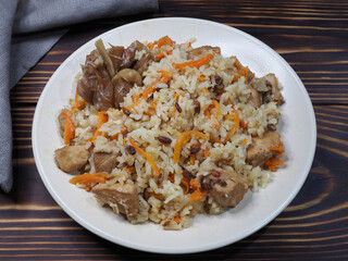 Traditional national dish pilaf. Garlic, carrots, rice, meat with seasonings and sauces in a plate on a wooden table, flat layout. Delicious Uzbek hot food plov with chicken, cereals and vegetables
