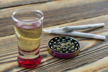 Joint, grinder, cannabis buds, alcohol shot and related items on a table.