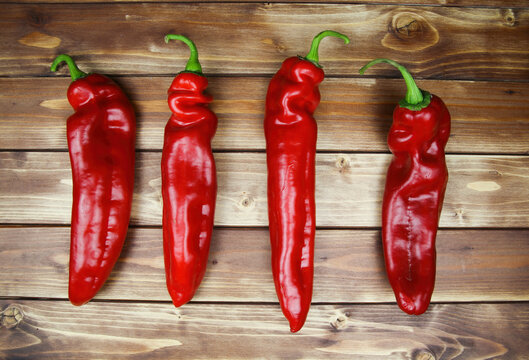 Closeup of isolated group 4 red ripe raw pointed peppers in a row, wood timber planks background