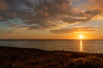 Coastline with sandy beach, heavy clouds and incoming waves during sunset