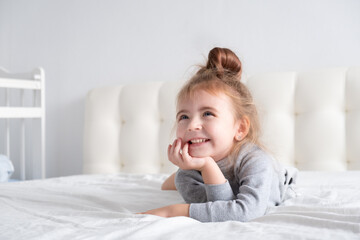 little girl in grey turtleneck having fun on white bedding