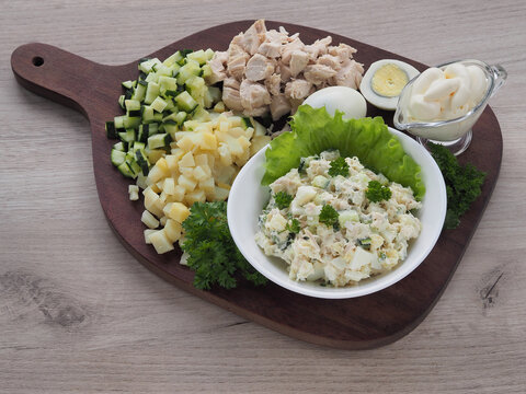 Mixed Salad With Vegetables And Meat In A Bowl, Sliced Potato Slices, Chicken Fillet, Fresh Cucumber, Chicken Egg, Mayonnaise, Spicy Herbs On A Kitchen Wooden Board. Recipe Of Traditional Olivier Sala
