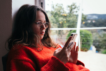Attractive pretty young woman in prescription glasses look at phone screen. Beautiful soft light...