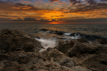 Red sunset, just swallowed by the sea. Warm colors like orange, red and yellow. The waves of the Mediterranean sea that crash on the rocks creating white foam.