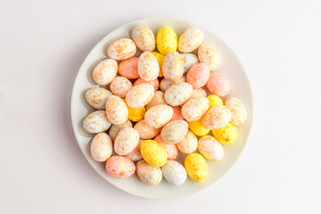 Mixed chocolate coated Easter eggs candies on a small plate isolated on a white table, tasty sugary dessert for children.